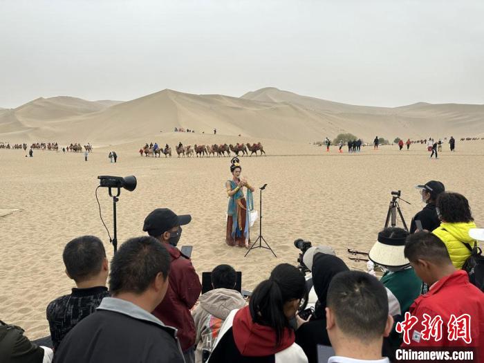 圖為2023年4月底，敦煌大漠“逐舞者”奧楠在鳴沙山月牙泉景區(qū)視頻直播，吸引游人圍觀?！●T志軍 攝